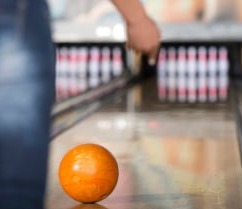 and person  throwing an orange bowling ball going down a lane
